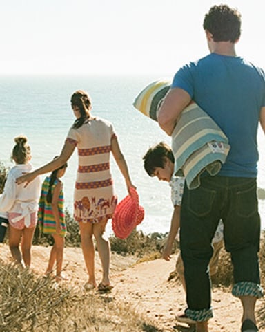 Family of five walking toward beach with towels and beach gear