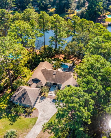 Aerial view of residential home with pool surrounded by tall pine trees and waterfront property